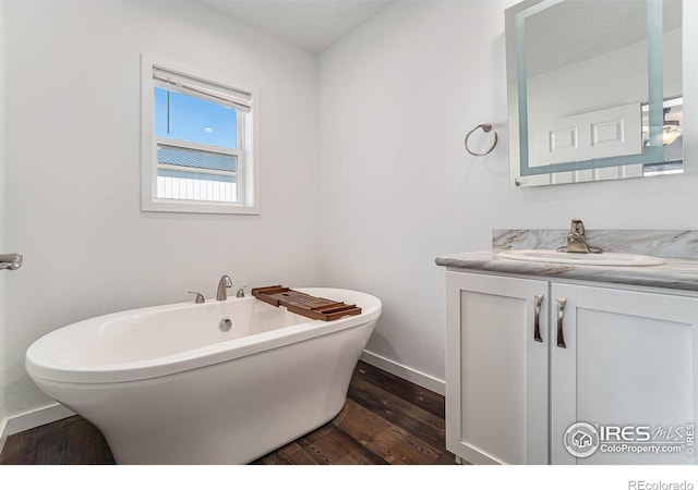 bathroom with a freestanding bath, vanity, baseboards, and wood finished floors