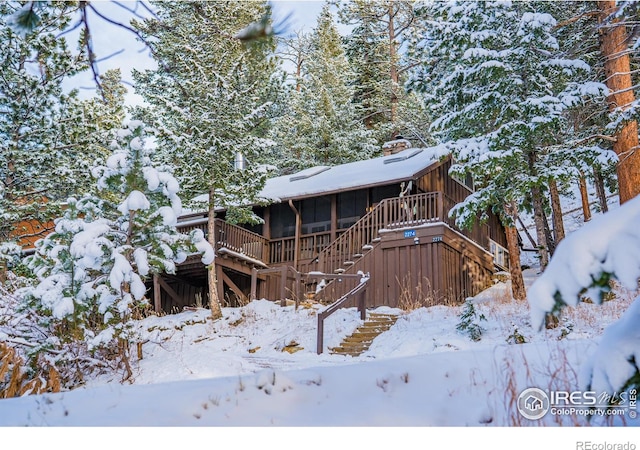 view of snow covered exterior with a chimney, a sunroom, a deck, and stairs