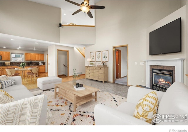 living room with light tile patterned floors, recessed lighting, a high ceiling, a glass covered fireplace, and ceiling fan