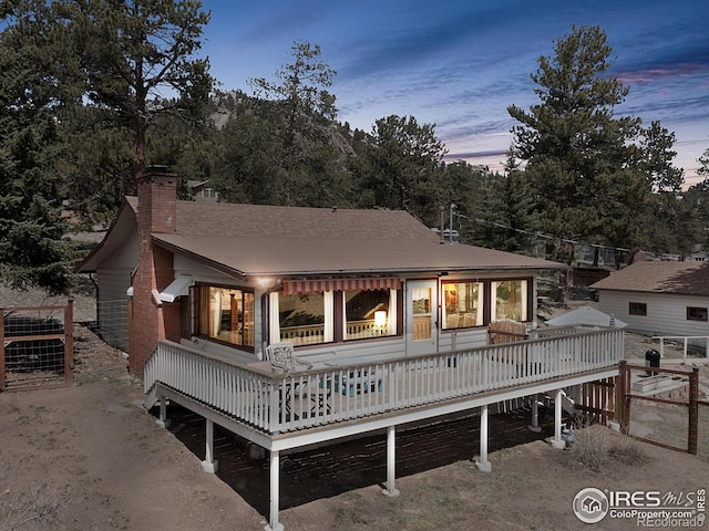 back of house at dusk with a deck and a chimney