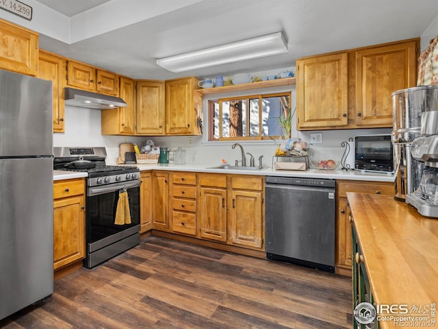 kitchen with under cabinet range hood, stainless steel appliances, butcher block countertops, a sink, and dark wood finished floors