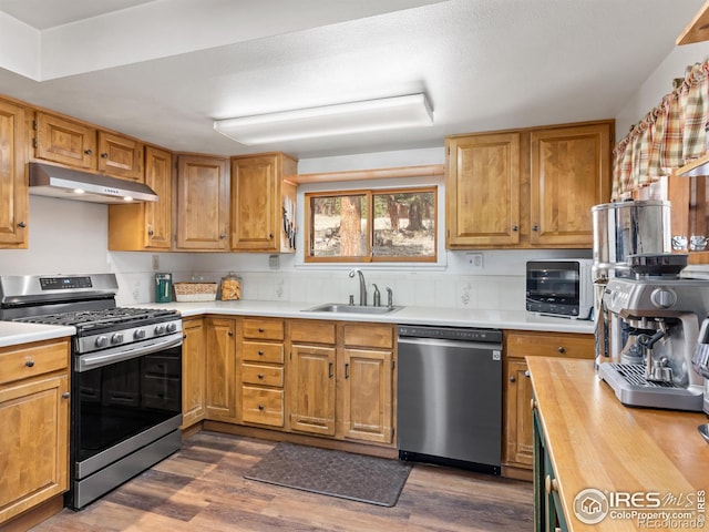 kitchen with dark wood-style floors, stainless steel appliances, a sink, wood counters, and under cabinet range hood