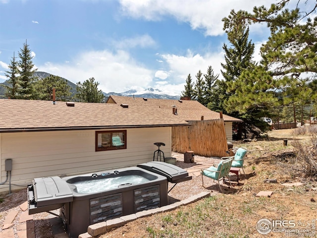 rear view of house featuring a hot tub, fence, a mountain view, and roof with shingles