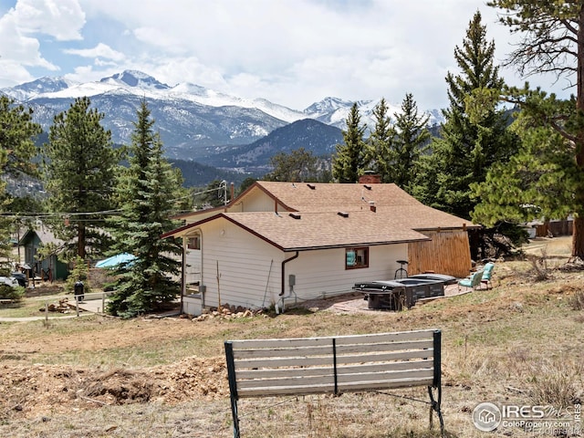 back of house with a fire pit, a shingled roof, a chimney, and a mountain view