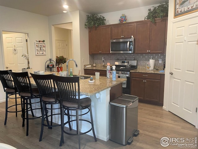 1431 Vantage Pkwy, Berthoud, CO 80513 - kitchen featuring appliances with stainless steel finishes, a sink, light wood-style flooring, a kitchen island with sink, and decorative backsplash