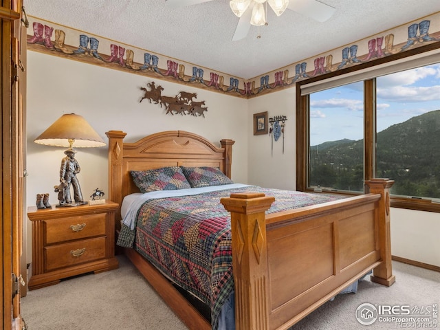 bedroom featuring light carpet, ceiling fan, a textured ceiling, and a mountain view