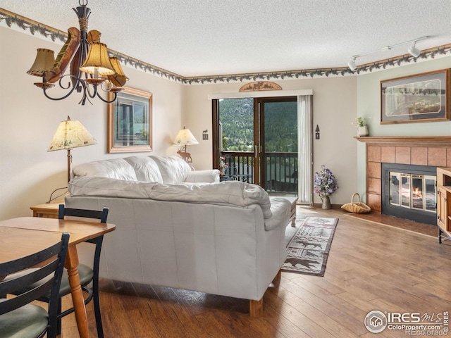 living room with wood-type flooring, a tiled fireplace, track lighting, and a textured ceiling