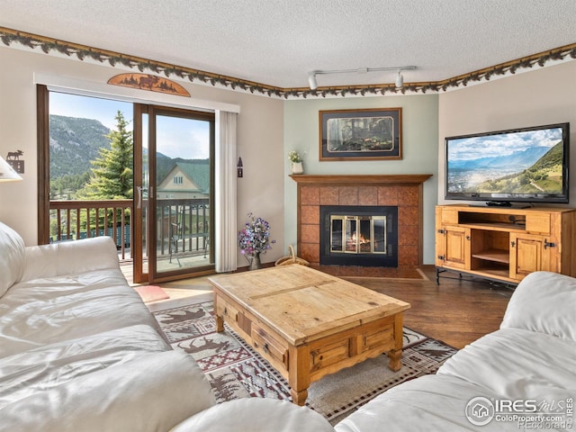 living area featuring a textured ceiling, track lighting, wood finished floors, and a tiled fireplace