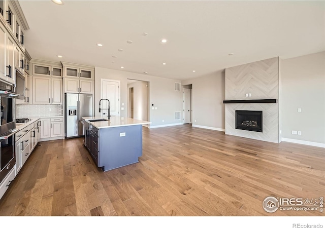 kitchen featuring a fireplace, stainless steel appliances, light wood-style flooring, a sink, and an island with sink