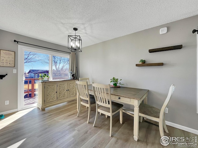 dining area with a textured ceiling, baseboards, light wood-style flooring, and an inviting chandelier