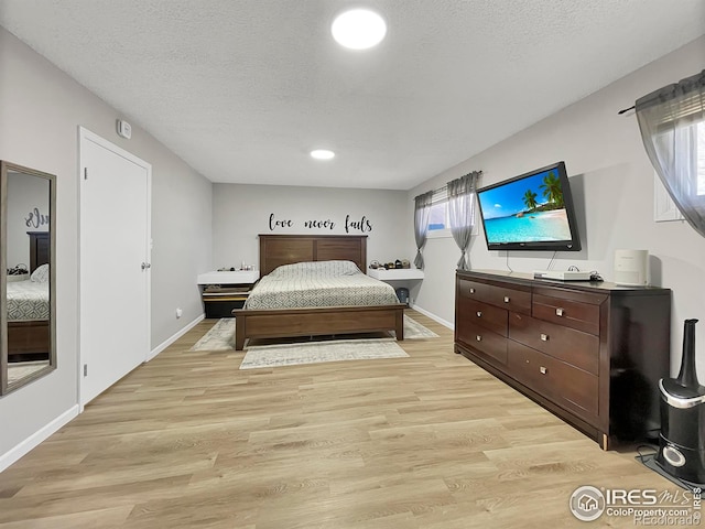 bedroom featuring light wood-type flooring, a textured ceiling, and baseboards