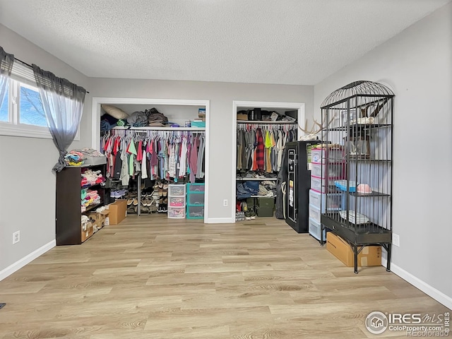 bedroom featuring a textured ceiling, baseboards, wood finished floors, and multiple closets