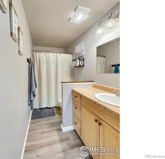 full bath with toilet, vanity, a textured ceiling, wood finished floors, and baseboards