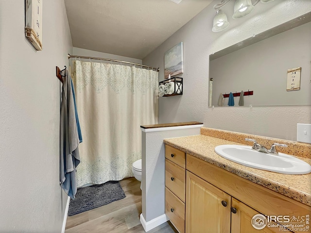 full bathroom with curtained shower, a textured wall, toilet, vanity, and wood finished floors