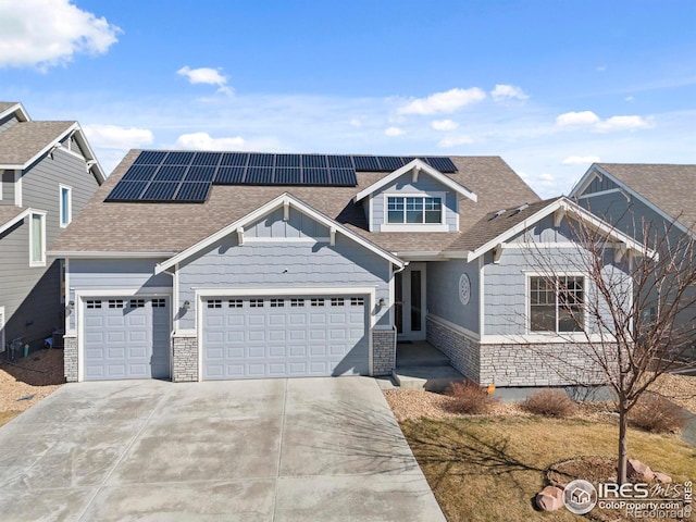 craftsman-style house featuring roof with shingles, solar panels, concrete driveway, a garage, and stone siding