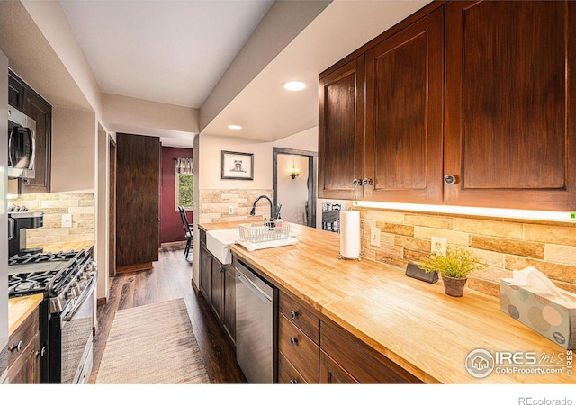 kitchen with decorative backsplash, dark wood-style floors, butcher block countertops, stainless steel appliances, and a sink