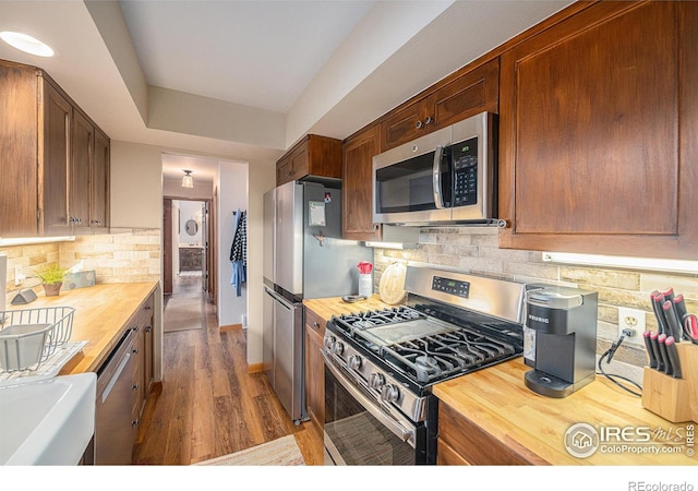 kitchen with stainless steel appliances, a raised ceiling, wooden counters, and decorative backsplash