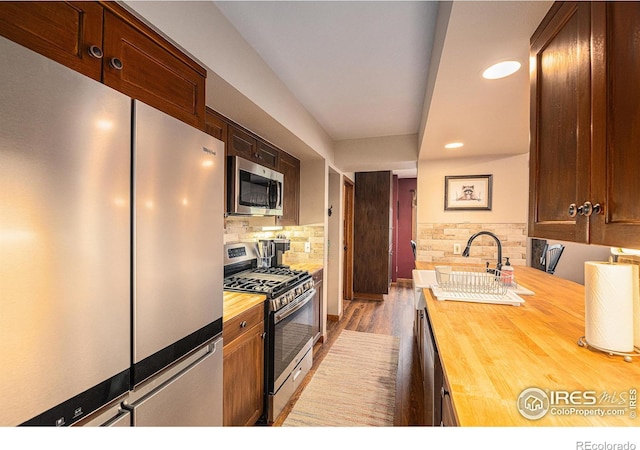 kitchen with stainless steel appliances, recessed lighting, wooden counters, decorative backsplash, and wood finished floors