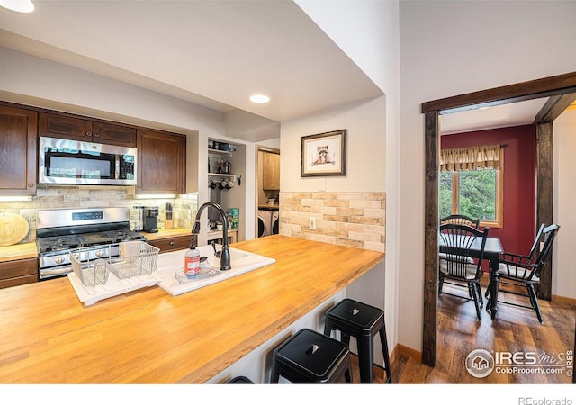 kitchen with wooden counters, appliances with stainless steel finishes, a breakfast bar area, and backsplash