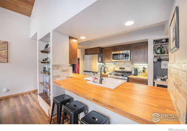 kitchen featuring stainless steel appliances, wooden counters, a peninsula, and a sink