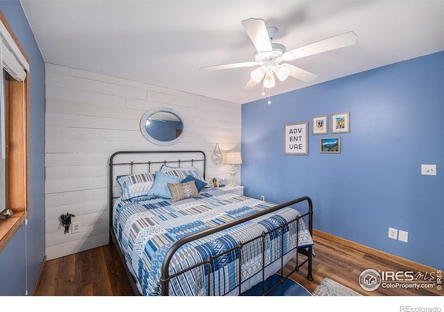 bedroom with wood walls, wood finished floors, and a ceiling fan