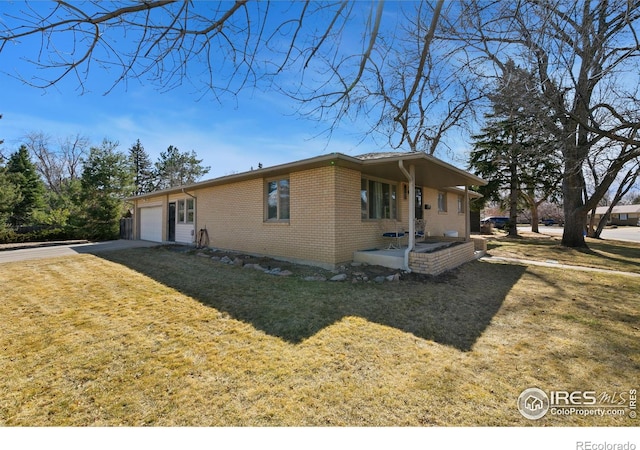 view of side of home featuring an attached garage, a yard, driveway, and brick siding