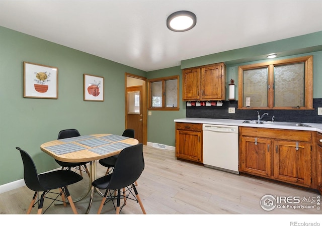 kitchen featuring light wood finished floors, brown cabinetry, white dishwasher, light countertops, and a sink