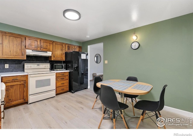 kitchen featuring white range with electric stovetop, brown cabinetry, black fridge with ice dispenser, stainless steel microwave, and under cabinet range hood