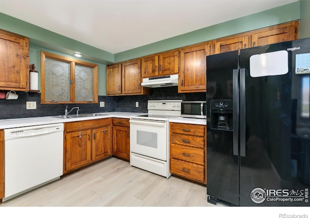 kitchen featuring under cabinet range hood, white appliances, a sink, brown cabinets, and tasteful backsplash