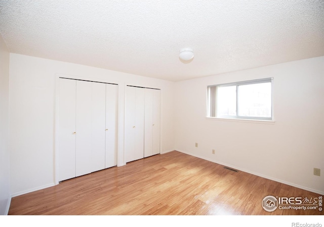216-218 E Saint Clair Ave, Longmont, CO 80504 - unfurnished bedroom with a textured ceiling, two closets, visible vents, and light wood-style floors
