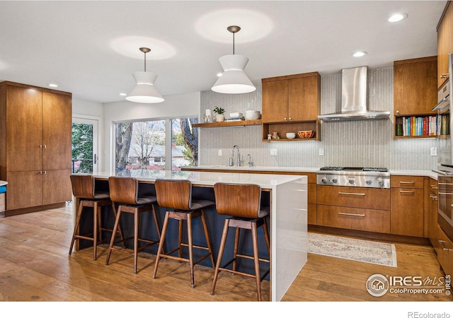 kitchen with light wood finished floors, wall chimney exhaust hood, brown cabinets, stainless steel gas cooktop, and open shelves