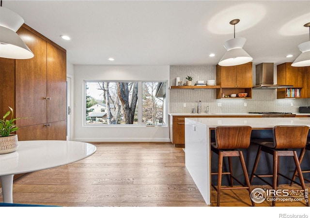 kitchen with open shelves, a sink, brown cabinets, wall chimney exhaust hood, and tasteful backsplash