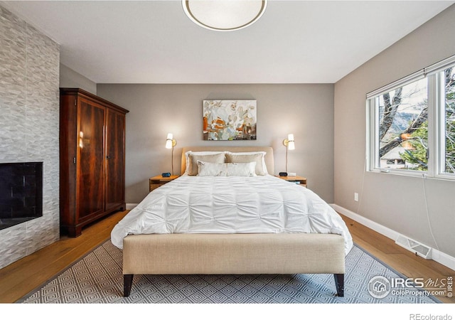 bedroom with a fireplace, wood finished floors, visible vents, and baseboards