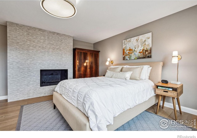 bedroom featuring a tiled fireplace, wood finished floors, and baseboards