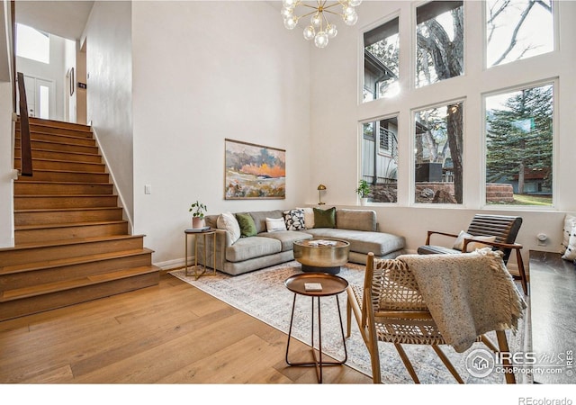 living room featuring a towering ceiling, an inviting chandelier, wood finished floors, baseboards, and stairs