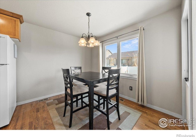 dining room featuring an inviting chandelier, wood finished floors, visible vents, and baseboards