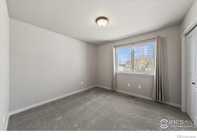 carpeted empty room with baseboards, visible vents, and a textured ceiling