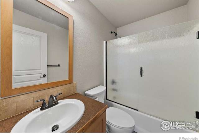 bathroom featuring shower / bath combination with glass door, tasteful backsplash, a textured wall, toilet, and vanity