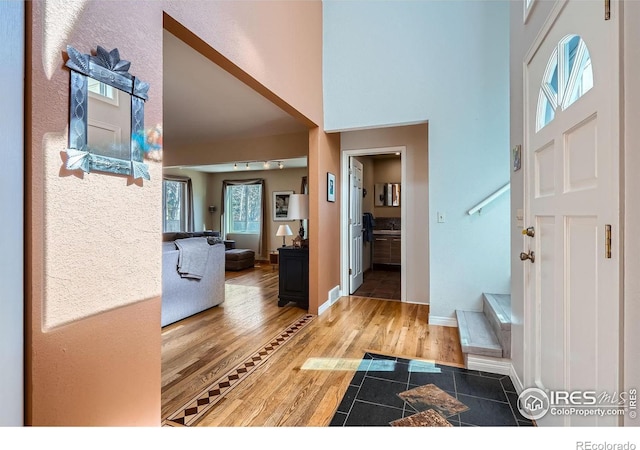 entryway featuring a towering ceiling, baseboards, stairway, and wood finished floors