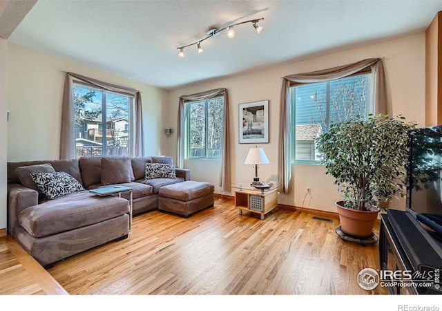 living room featuring rail lighting, visible vents, a textured ceiling, wood finished floors, and baseboards