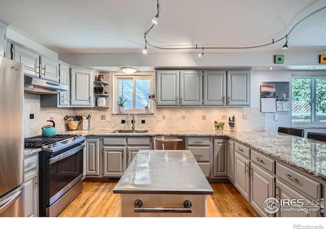 kitchen featuring a wealth of natural light, gray cabinets, stainless steel appliances, under cabinet range hood, and a sink