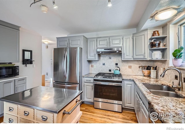 kitchen with stainless steel appliances, gray cabinetry, light wood-type flooring, under cabinet range hood, and a sink