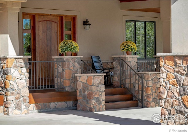 property entrance featuring stucco siding, covered porch, and stone siding