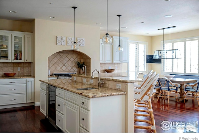 kitchen with a sink, dark wood-type flooring, glass insert cabinets, backsplash, and recessed lighting