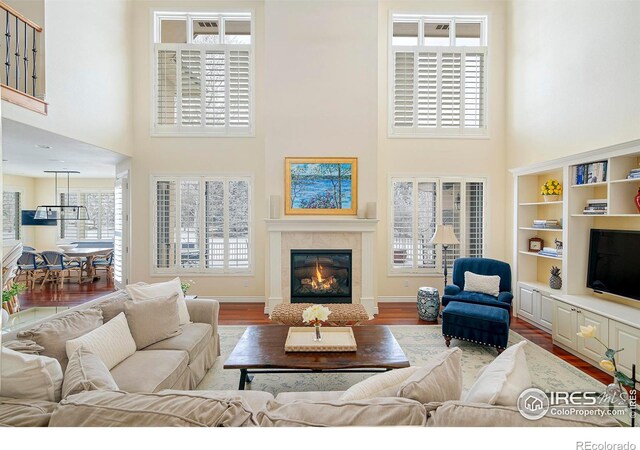 living area featuring a high ceiling, wood finished floors, a glass covered fireplace, and baseboards