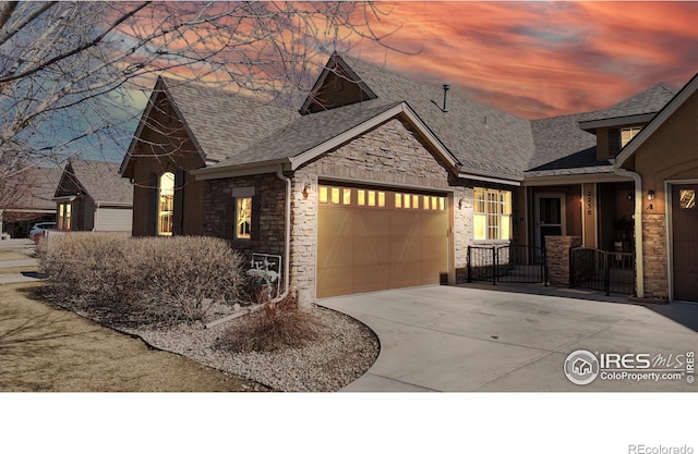 view of front of home with stone siding, driveway, a garage, and roof with shingles