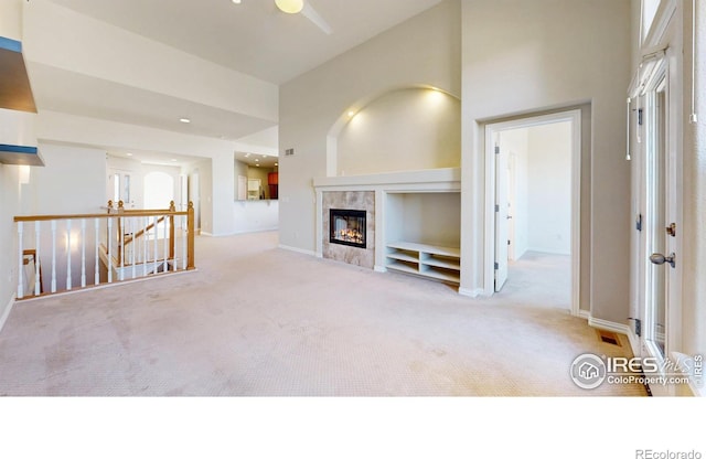 unfurnished living room with carpet floors, a high ceiling, baseboards, and a tile fireplace