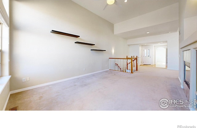 unfurnished room featuring carpet floors, a glass covered fireplace, a ceiling fan, and baseboards