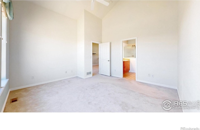 unfurnished bedroom featuring high vaulted ceiling, a walk in closet, visible vents, and light colored carpet