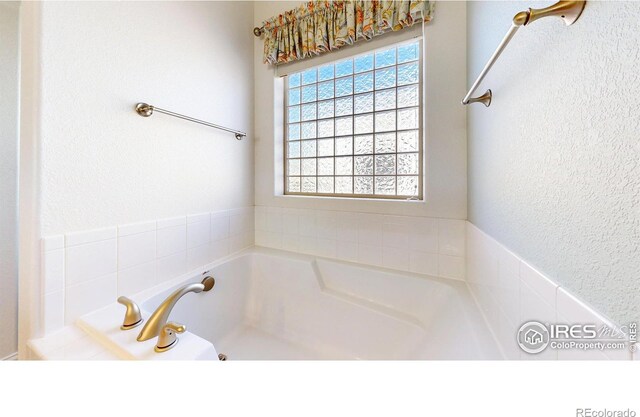 full bath featuring a garden tub and a textured wall